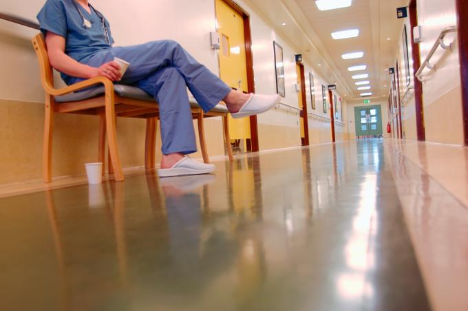 A female doctor sitting on a chair in an empty hospital hall with two empty cups of coffee.